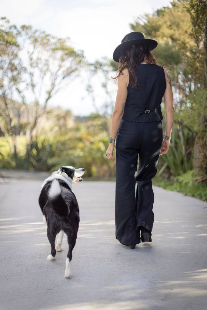 Person walking a black and white dog on a path with trees in the background