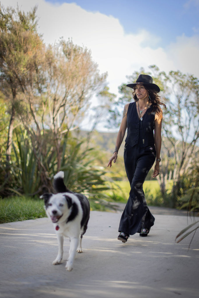 Woman in black outfit walking a dog on a path with trees and grass in the background