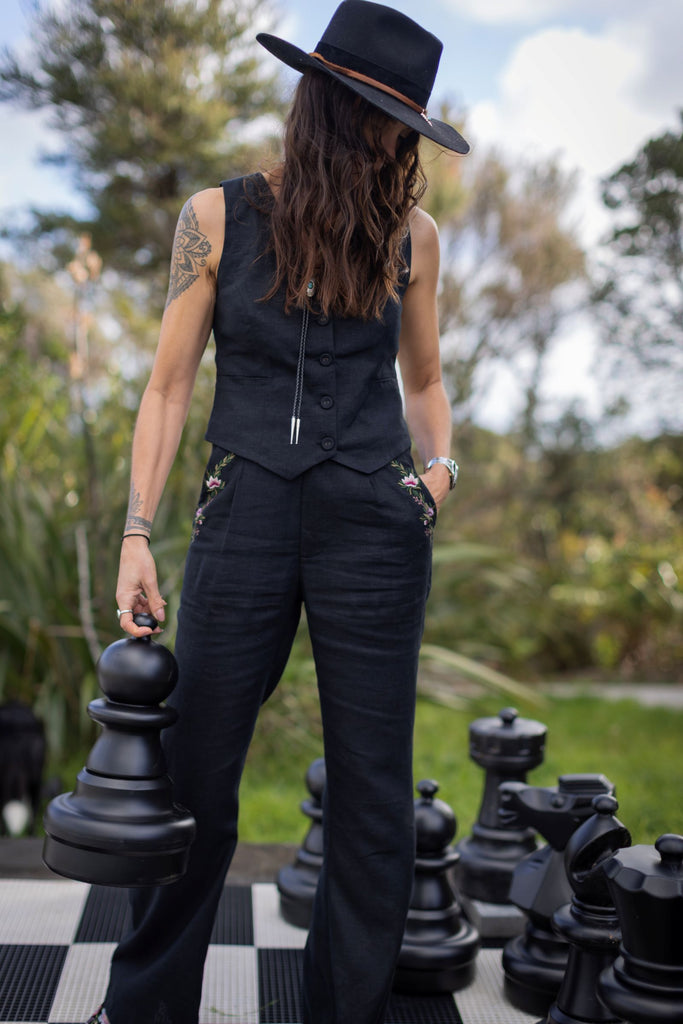 Person in black outfit standing on a giant chessboard with large chess pieces outdoors.