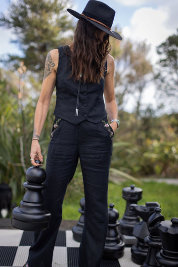 Person in black outfit standing on a giant chessboard with large chess pieces outdoors.