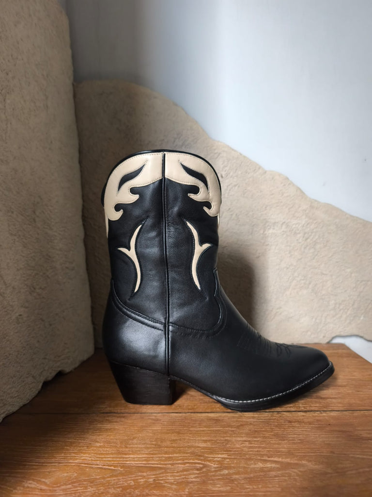 Black cowboy boot with white stitching on a wooden surface