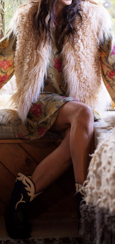 Person wearing a fluffy beige coat sitting on a patterned couch.