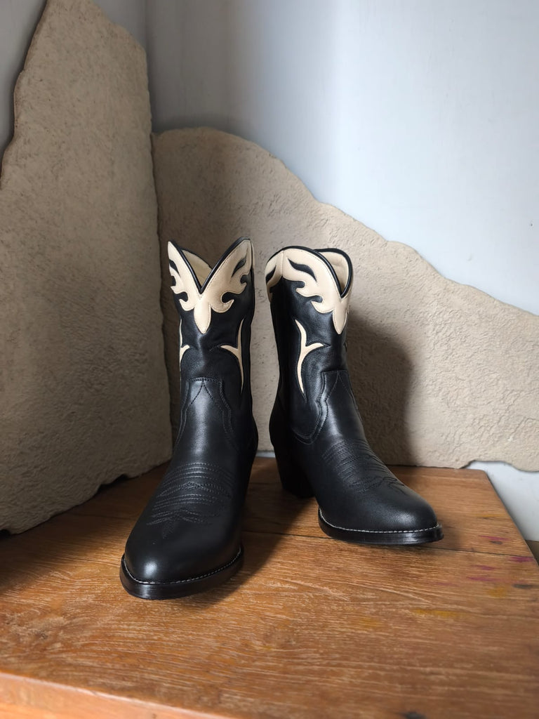 Black cowboy boots with white butterfly designs on a wooden surface.