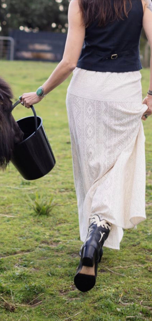Person wearing a long white skirt and black cowboy boots on grass
