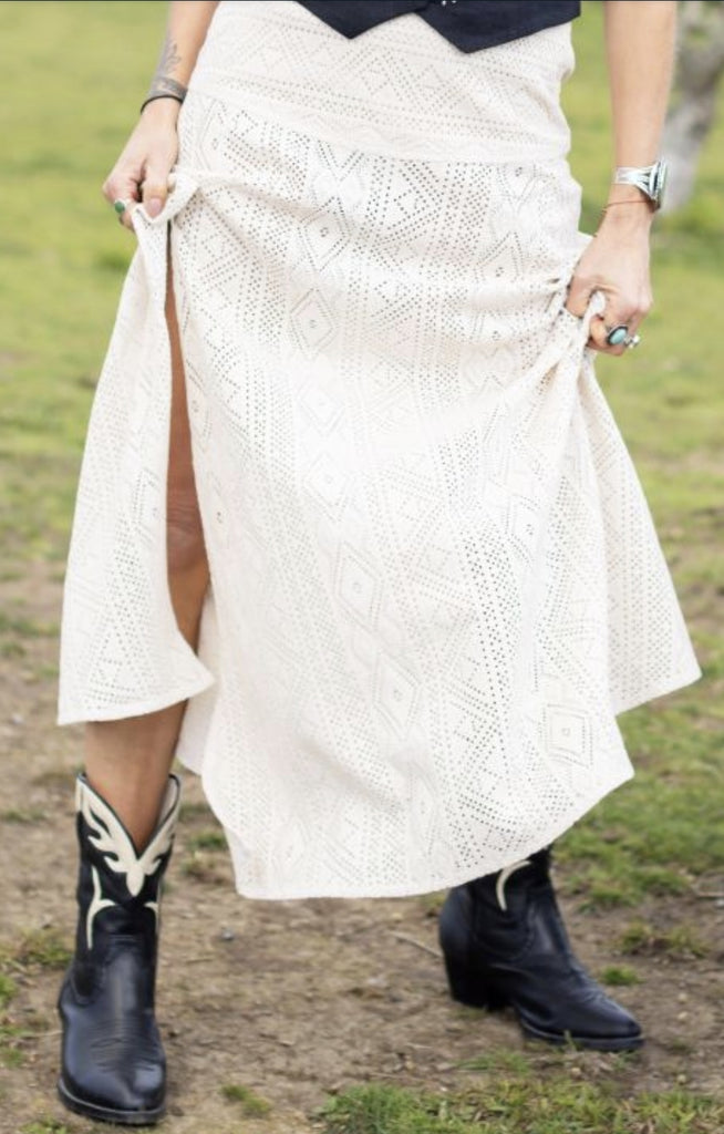 Person wearing a white lace skirt with a high slit, standing on grass in her cowboy boots