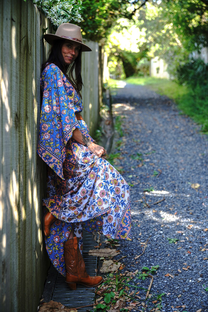 Lifestyle photo of a woman leaning against a fence wearing the Wildflower Kaftan, showing the floral print and relaxed bohemian styling