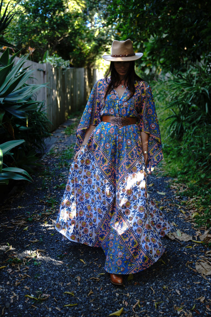 Woman walking outdoors wearing the Wildflower Organic Cotton Kaftan, lifting the skirt slightly to show the flowing movement of the blue and peach floral print
